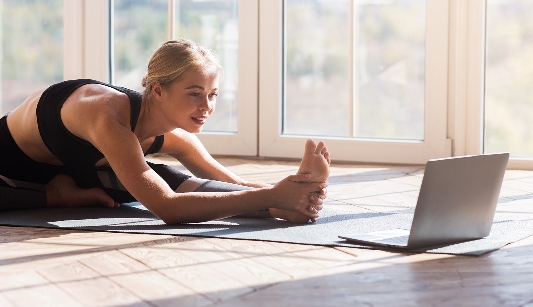 Flexible girl doing yoga at home, looking at laptop screen