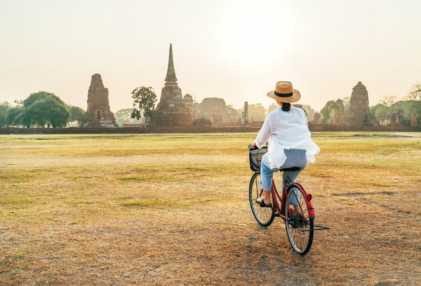 Woman riding bicykle near Ayutthaya historical park in Thailand, early morning time